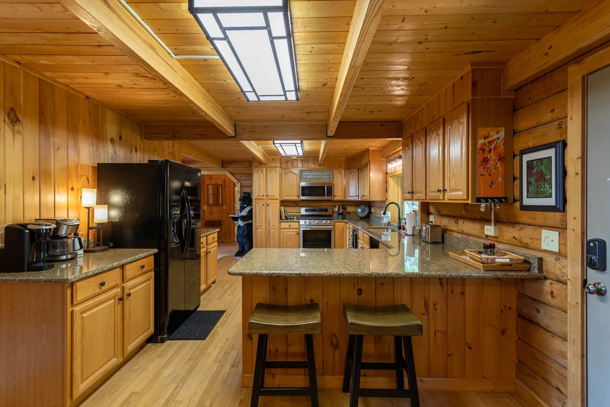 This image offers a clear view of the kitchen, featuring granite countertops, warm wood cabinetry, a black refrigerator, and a kitchen island. The space is well-lit and practical, perfect for group cooking or casual chats while preparing meals together.