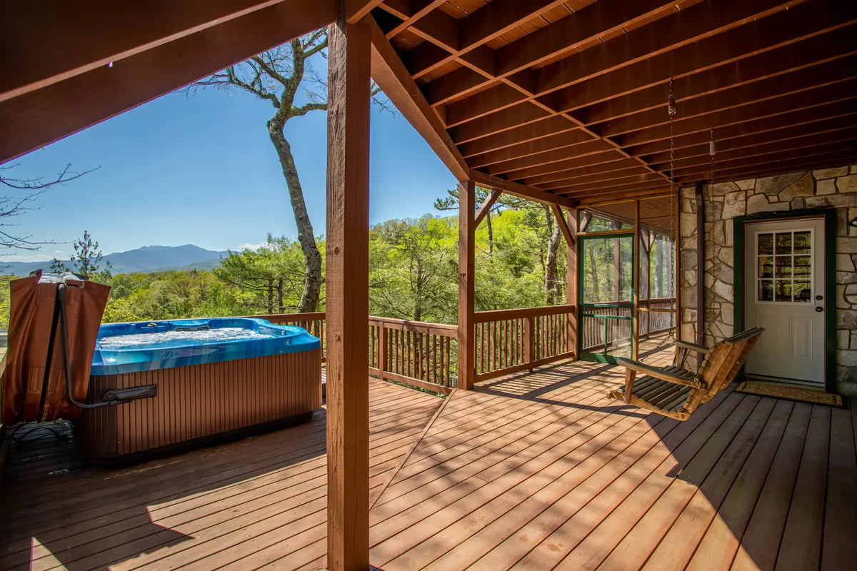 A scenic wooden deck with a bubbling hot tub, a wooden swing, and an open view of the surrounding mountains. The arrangement invites relaxation, with nature as the backdrop, and the hot tub positioned to maximize the view.