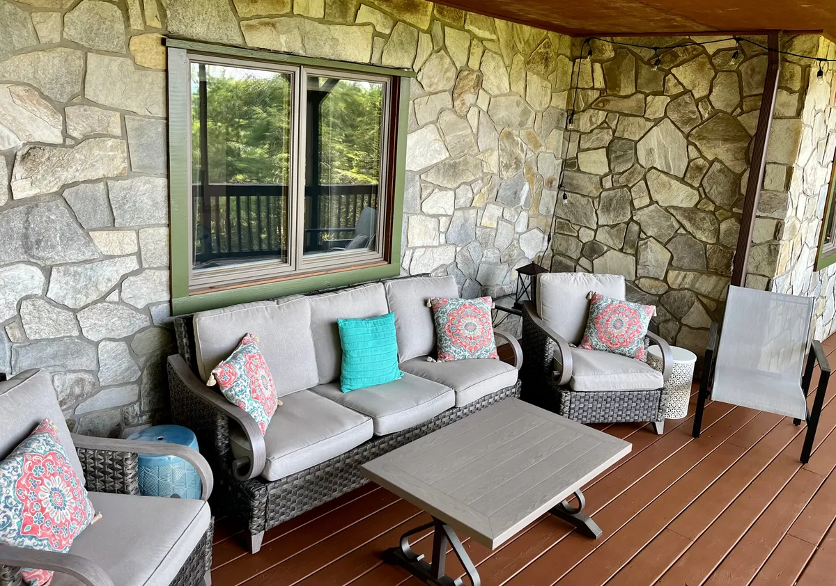 Comfortable outdoor seating with plush pillows is arranged on a stone-walled patio, offering a serene space for reading, socializing, or simply soaking up the peaceful surroundings. The greenery and natural setting enhance the sense of sanctuary.