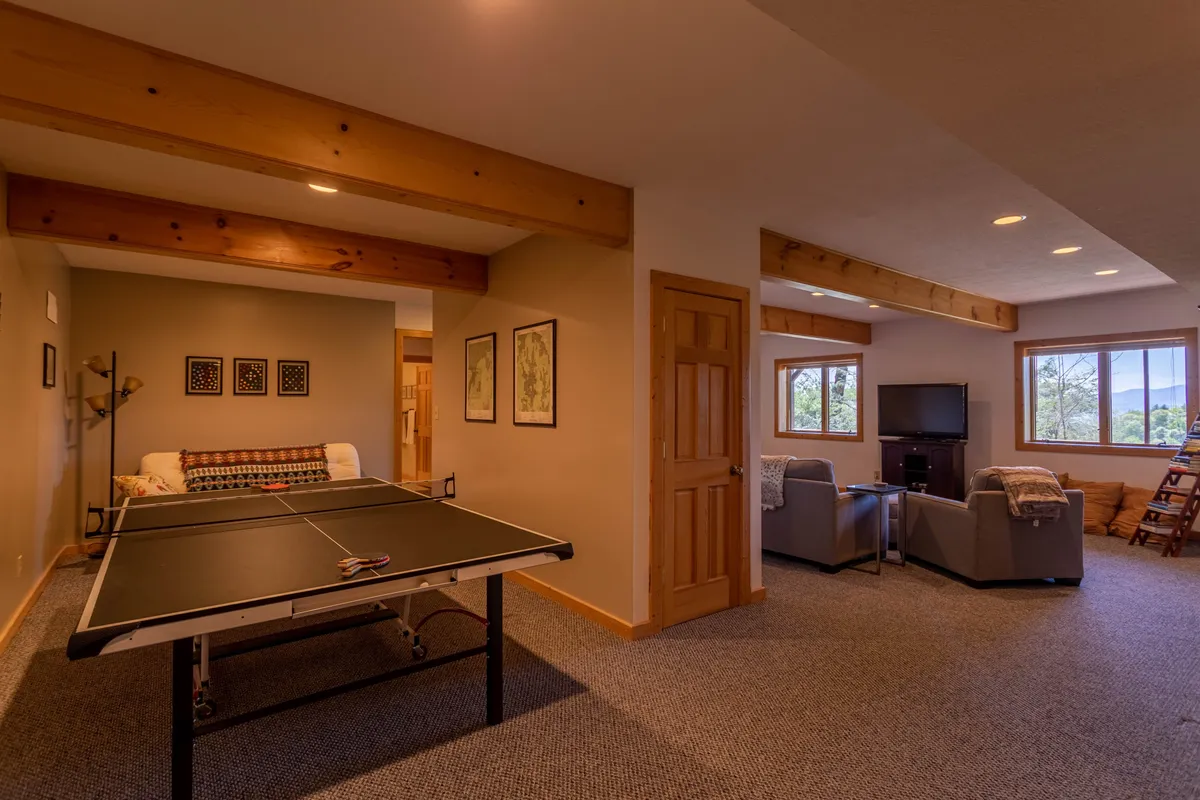 This image captures a spacious game room featuring a ping pong table as the centerpiece, surrounded by comfortable seating and large windows that invite natural light. Decorative artwork on the walls adds a playful touch, while the layout encourages friendly competition and group gatherings.