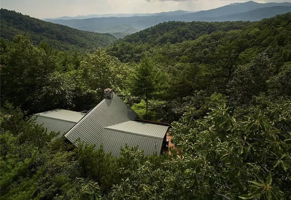 This wide-angle exterior highlights the house’s unique roof structure, surrounded by lush greenery and a distant mountain range. It evokes the sense of expansive, private land ideal for outdoor play, exploration, and stargazing.