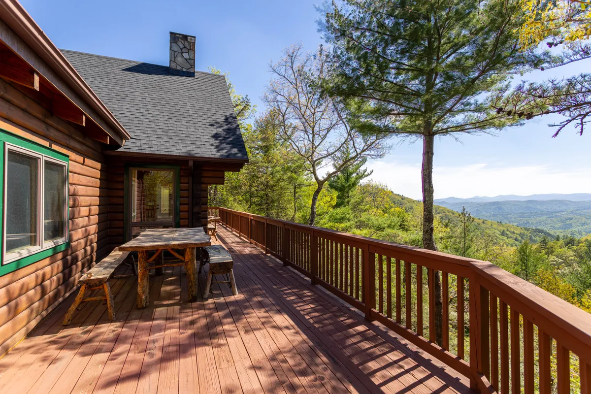 This image shows a spacious wooden deck attached to the cabin, overlooking a breathtaking mountain view. The deck features ample open space, inviting guests to relax, work, or take in the scenery. The log cabin structure and natural surroundings emphasize the property’s connection to nature and seclusion.